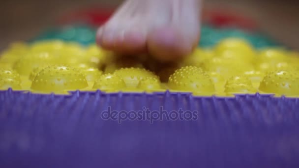 La chica camina sobre una alfombra de masaje de rompecabezas de diferentes colores — Vídeo de stock