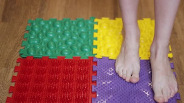 The girl walks on a massage mat from puzzles of different colors — Stock Video