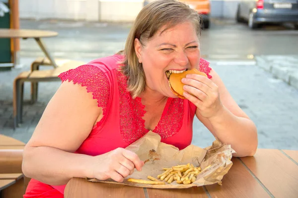 Silná žena jíst fast food hamburger a hranolky v kavárně — Stock fotografie