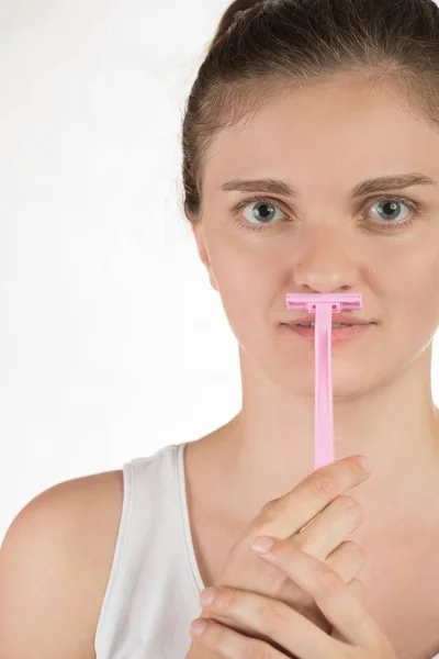 Young woman shaves a mustache on her face with a pink razor on a — Stock Photo, Image