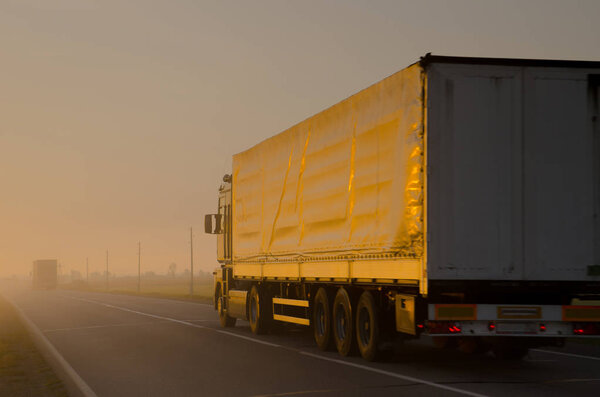 A truck is driving along the summer road in the morning in a thi