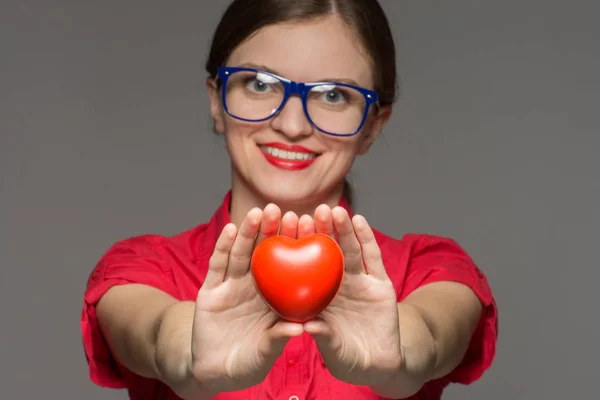 Bella ragazza bruna in occhiali sorride e tiene un cuore in h — Foto Stock