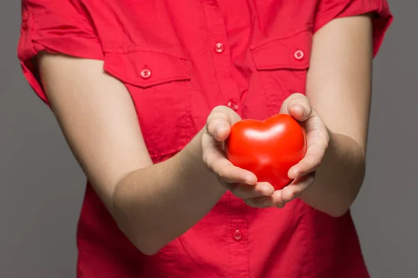 Una ragazza tiene un cuore rosso tra le mani su uno sfondo grigio — Foto Stock