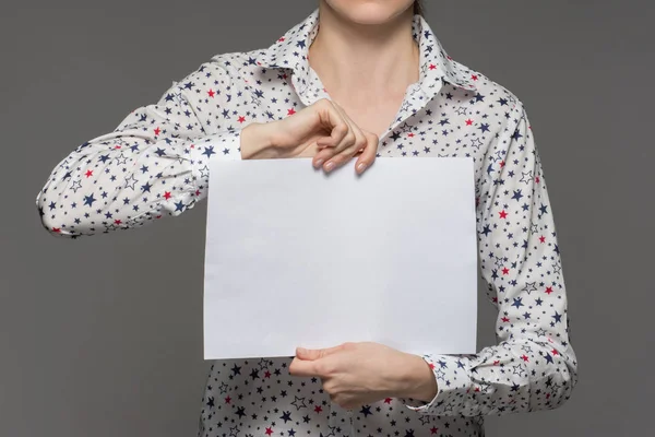 Une fille tient une feuille blanche de papier dans ses mains sur un dos gris — Photo
