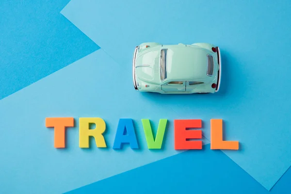 Green toy car and inscription plastic travel letters on a blue b — Stock Photo, Image