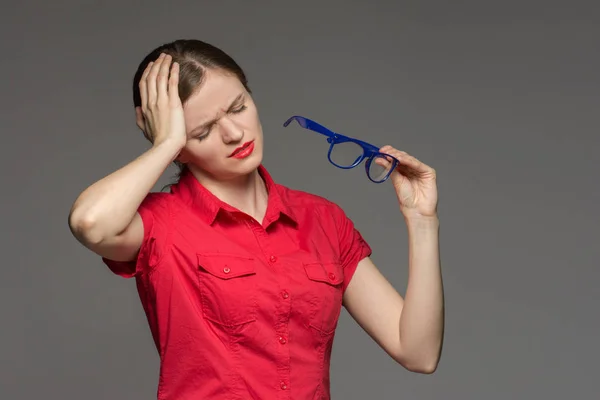 Mooie jonge meisje in een rode shirt zere ogen van glas heeft — Stockfoto