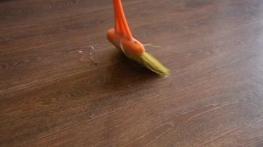 Kadın bir turuncu fırça ve süpürge ile evde yerdeki toz süpürür ve düzen ve temizlik getiriyor