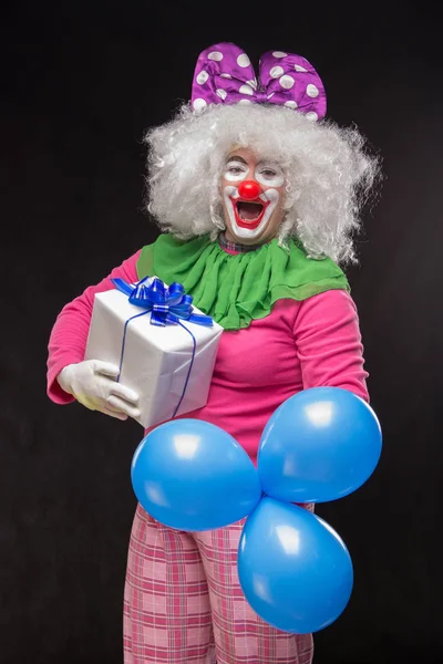 Funny clown with hair and a cheerful make-up holding a gift on a — Stock Photo, Image