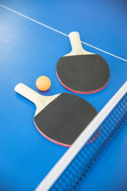 Masa tenisi için turuncu top ve iki ahşap raket kırmızı ve siyah renkli bir masa üzerinde ızgara ile