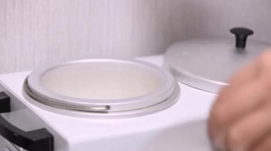 Karıştırmak için beyaz balmumu hazırlığı. Saydam tıbbi eldivenli sürgün ustası tavaya balmumu koyar.