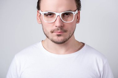 Gözlüklü ve beyaz tişörtlü yakışıklı bir adam şüpheli görünüyor.