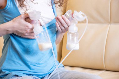 Ellerinde göğüs pompası olan genç bir anne kanepede oturur..