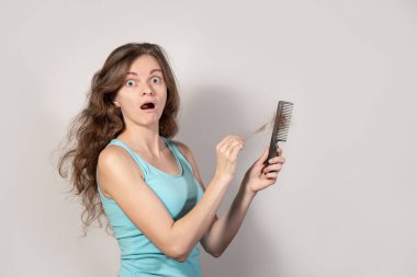 Endişeli esmer kız gri bir arka planda kayıp kıvırcık saçlı siyah bir tarak tutuyor.