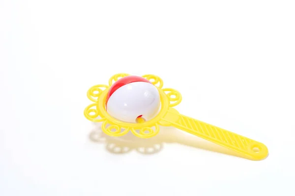 Yellow plastic rattle for a baby in the form of a flower with a handle on a white background