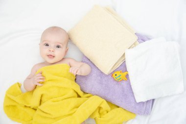 Beyaz bir bez üzerinde banyodan sonra sarı bir havluyla güzel, neşeli küçük bir bebeğin portresi.