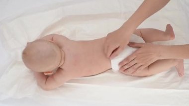 Genç anne, yeni doğmuş bebeğine beyaz bir bezle masaj yapıyor.