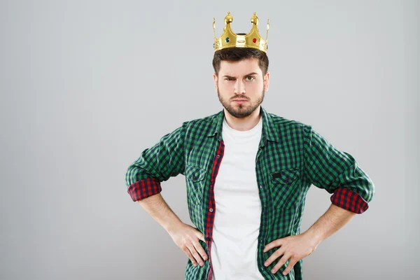 Frowning young man in green checked shirt and crown — Stock Photo, Image