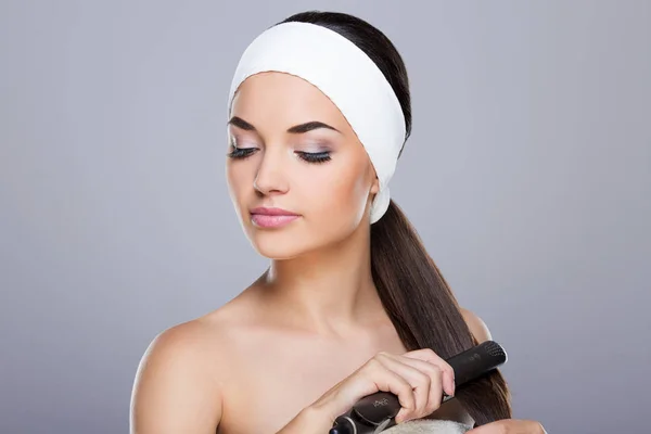 Mujer joven alisando el cabello — Foto de Stock