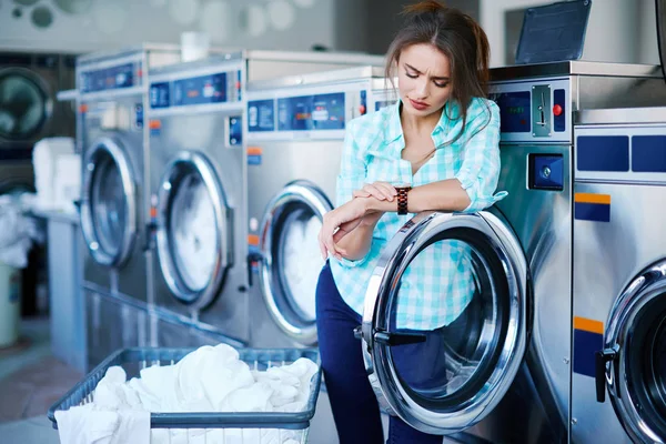 Girl looking at watch near washing machines — Stock Photo, Image
