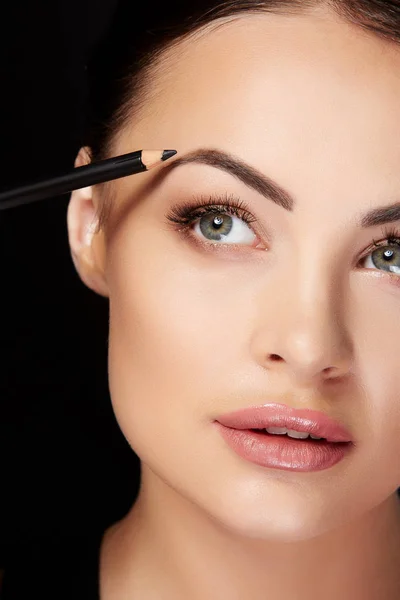 Young woman painting eyebrows with black pencil