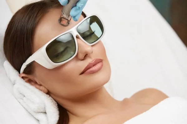 美容室で保護眼鏡をかけて額にレーザー手術をする美人女性のクローズアップ — ストック写真