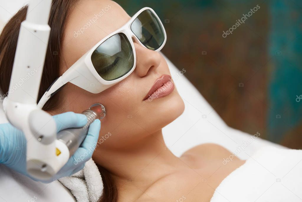 pretty woman receiving face treatment with laser wearing protection glasses, girl having cosmetic procedure in spa clinic