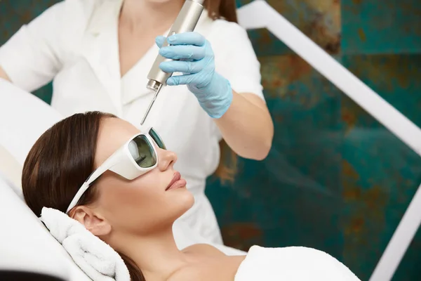 Bella ragazza sdraiata nel salone di bellezza e ricevere la terapia laser per la fronte indossando occhiali di protezione — Foto Stock