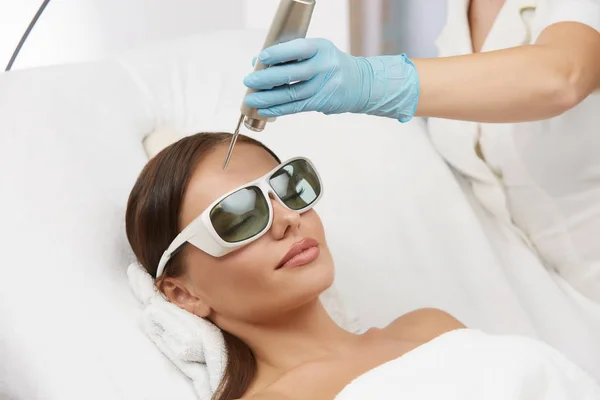 Woman receiving laser theraphy for forehead wearing protection glasses — 스톡 사진