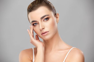 Mükemmel makyajlı güzel bir kadın yüzüne dokunuyor ve kameraya bakıyor.