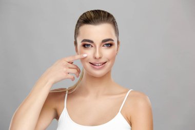 Güzel kız yanağına tek parmakla dokunuyor ve kameraya gülümsüyor.