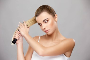 Güzel kız uzun açık renk saçlarını tarıyor ve fırçaya bakıyor.