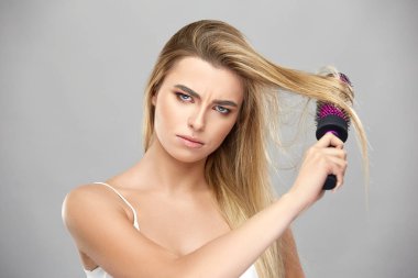 Kızgın kadın uzun sarı saçlarını tarıyor ve öfkeyle kameraya bakıyor.