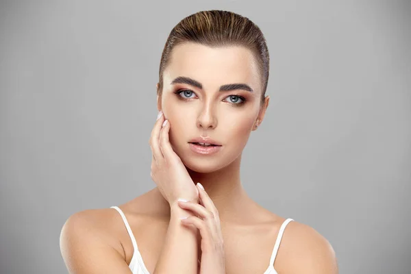 Modelo feminino atraente com maquiagem leve e cabelo apertado atrás olhando para a câmera e tocando o rosto com o braço — Fotografia de Stock