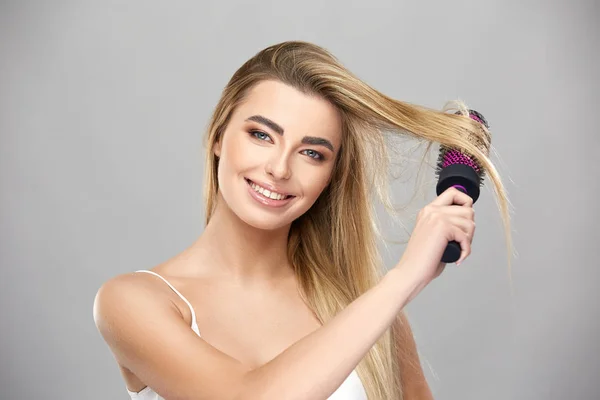 pretty girl brushing hair isolated on grey background and smiling to camera