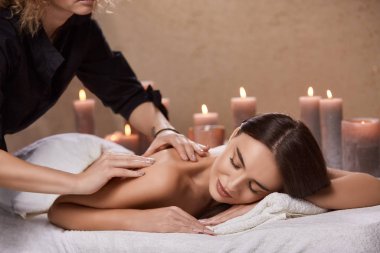 masseur doing massage for woman's back in spa salon with many candles, female having relaxation and body treatment by beautician 