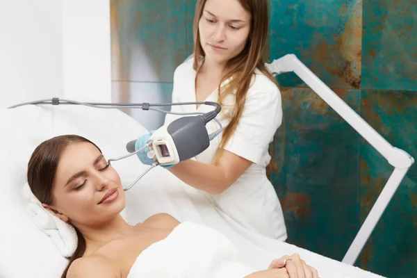 lovely lady with perfect face doing cosmetology procedures with laser by beautician, pretty woman receiving facial hair removal