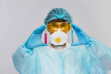 Bioxazard kostümlü doktor kameraya iki farklı test tüpü gösteriyor.