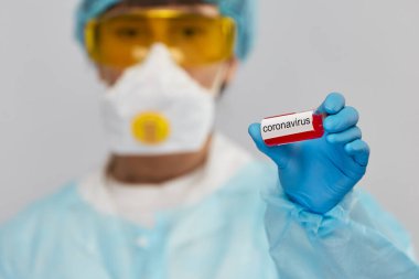 Biyolojik tehlike taşıyan doktor deney tüpünde koronavirüs örneği tutuyor. Antivirüslü genç bilim adamı COVID-19 'a.