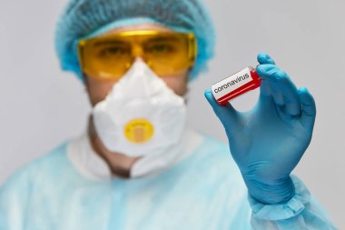 Sarı koruyucu gözlüklü tek kullanımlık maske ve mavi eldivenli doktor Coronavirus test tüpü taşıyor.
