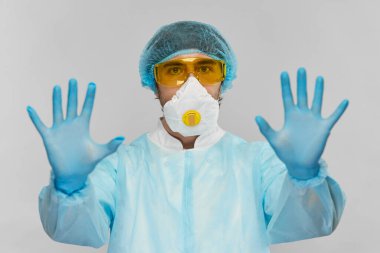 Protoaktif giysili biyokimyacı sarı gözlükler raspiratuar maskeli ve mavi tek kullanımlık eldivenli dur işaretini kameraya doğrultmuş.