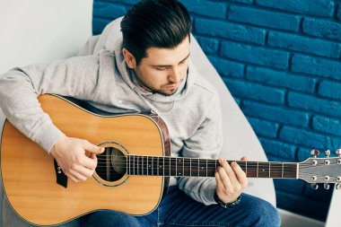 Arka planda mavi duvarla gitar çalan yakışıklı adamın yakın çekimi.