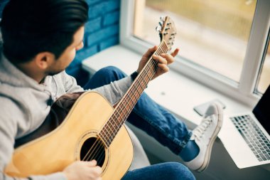 Gitaristin elinde gitaristin yakın plan fotoğrafı ve pencere kenarında dizüstü bilgisayarla oturması.
