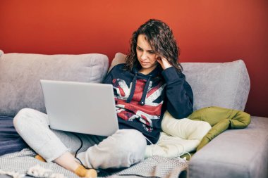 Karantinada rahat giysiler içinde dizüstü bilgisayar kullanan kıvırcık esmer.