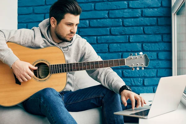 Modern tasarım dairesinde oturan ve dizüstü bilgisayar kullanan bir gitarist.