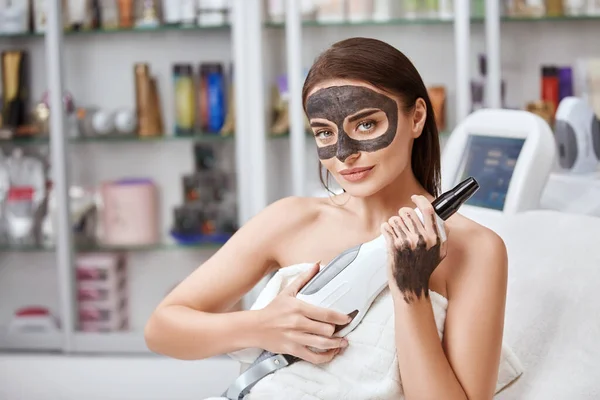 pretty woman with carbon mask on face holding laser machine like a pistol and looking to camera, copy space, facial care , beauty concept