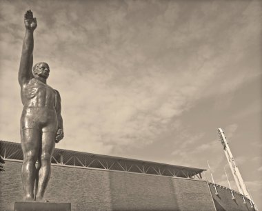 AMSTERDAM NETHERLANDS 02 10 2015: Sculpture by Gra Rueb Official Olympic Salute Stopped Being Popularly Used After WWII Due to Strongly Resembling the Heil Hitler Salute. In front the olympic stadium clipart