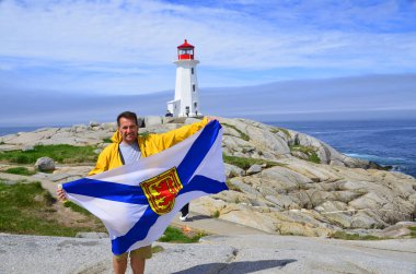 PEGY 'İN Koyu NOVA SCOTIA 6 Haziran: 6 Haziran 2014' te St. Margarets Körfezi 'nin doğu kıyısında bulunan Peggy' nin Koyu 'nun deniz fenerinin önünde Nova Scotia bayrağı sallayan adam.