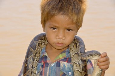 SIEM REAP CAMBODIA - 26 Mart 2013 'te Siem Reap Kamboçya' da para için pitonla poz veren kimliği belirsiz bir çocuğun portresi. Kamboçyalıların yaklaşık% 34 'ü günde bir dolardan az parayla hayatta kalıyor.. 