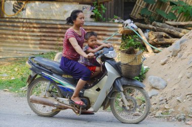VANGVIENG LAOS APRIL - 2 2013: Motosikletli anne ve çocuk laos hmong portresi. Laos nüfusunun yarısından fazlası yoksulluk sınırının altında yaşıyor..