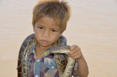 SIEM REAP CAMBODIA - 26 Mart 2013 'te Siem Reap Kamboçya' da para için pitonla poz veren kimliği belirsiz bir çocuğun portresi. Kamboçyalıların yaklaşık% 34 'ü günde bir dolardan az parayla hayatta kalıyor.. 
